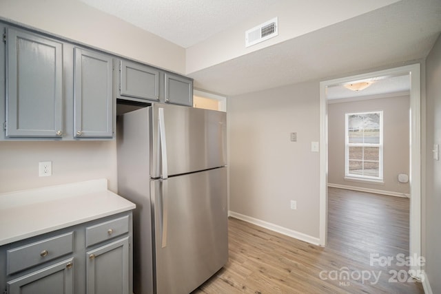 kitchen with gray cabinetry, stainless steel fridge, a textured ceiling, and light wood-type flooring