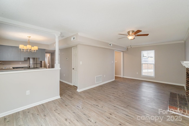 unfurnished living room with ornate columns, ceiling fan with notable chandelier, ornamental molding, light hardwood / wood-style floors, and a brick fireplace