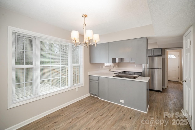 kitchen featuring gray cabinets, stainless steel fridge, hanging light fixtures, kitchen peninsula, and light hardwood / wood-style flooring