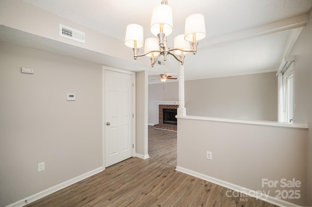 unfurnished dining area featuring a brick fireplace, ceiling fan with notable chandelier, and wood-type flooring