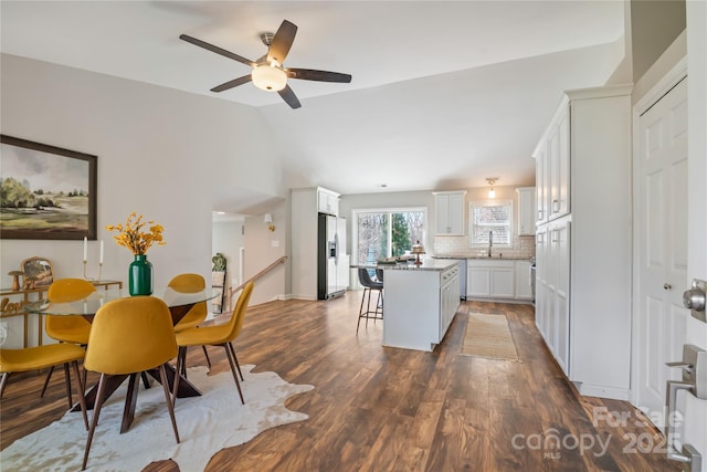 kitchen with stainless steel refrigerator with ice dispenser, lofted ceiling, a kitchen island, a sink, and a kitchen breakfast bar