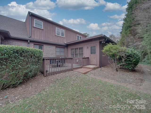 back of property featuring brick siding, a lawn, and a deck