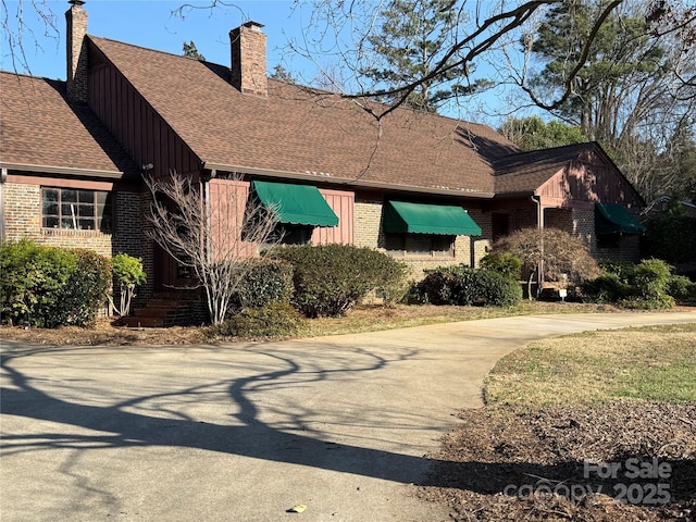 view of front of property featuring roof with shingles, brick siding, a chimney, and concrete driveway