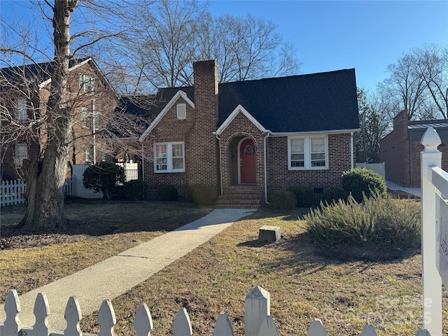 english style home with brick siding, fence, crawl space, a front lawn, and a chimney