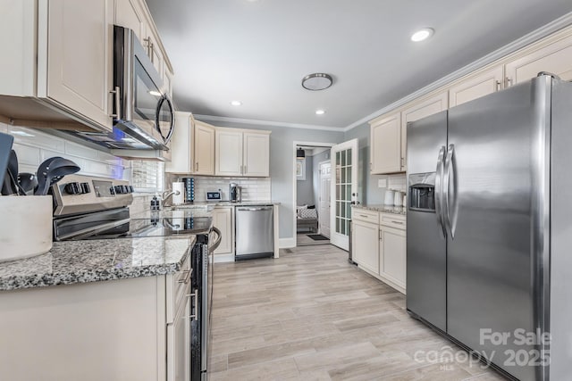 kitchen featuring crown molding, tasteful backsplash, stainless steel appliances, light stone countertops, and cream cabinets