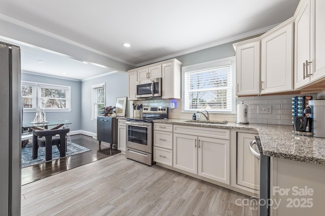 kitchen featuring sink, appliances with stainless steel finishes, light stone counters, white cabinets, and light wood-type flooring