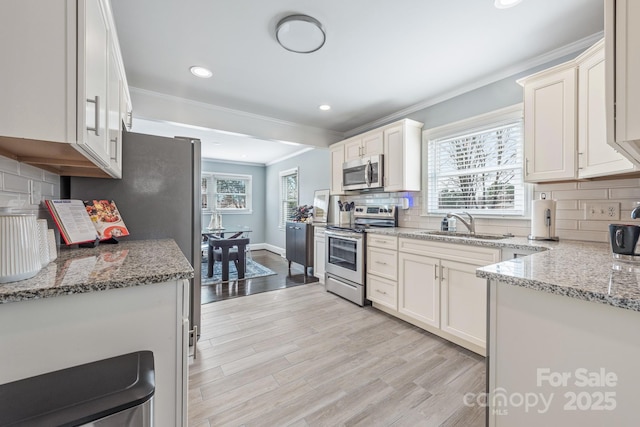 kitchen with sink, light stone counters, ornamental molding, stainless steel appliances, and light hardwood / wood-style floors