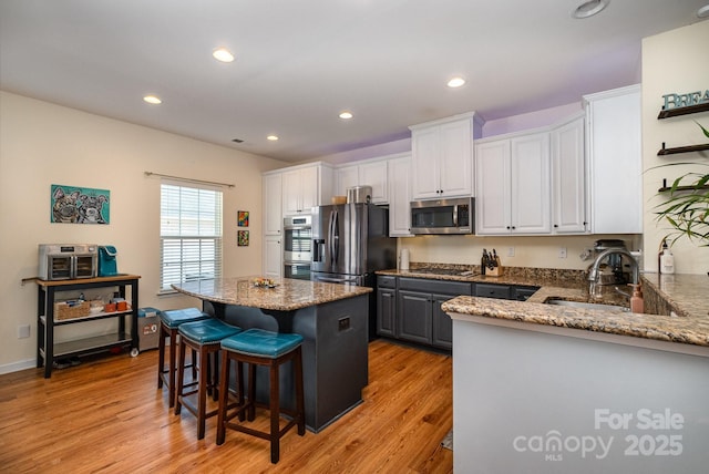 kitchen with white cabinets, light wood-style floors, appliances with stainless steel finishes, a breakfast bar, and a kitchen island