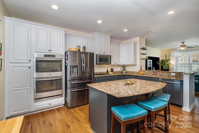 kitchen featuring a peninsula, white cabinets, stainless steel appliances, light stone countertops, and a kitchen breakfast bar