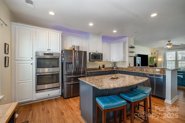 kitchen with a kitchen bar, a peninsula, white cabinets, and appliances with stainless steel finishes