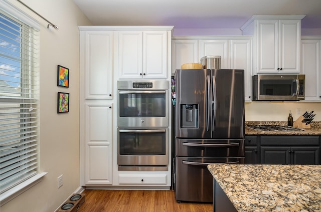 kitchen with appliances with stainless steel finishes, white cabinets, light stone counters, and light wood finished floors