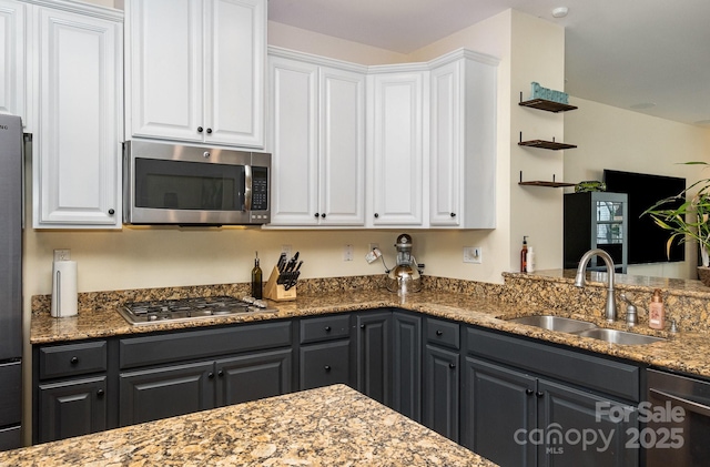 kitchen with white cabinetry, stainless steel appliances, light stone counters, and a sink