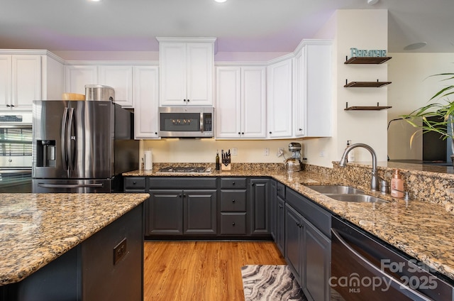 kitchen with appliances with stainless steel finishes, white cabinets, a sink, and dark stone countertops