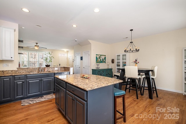 kitchen featuring decorative light fixtures, light wood-type flooring, white cabinetry, a sink, and a kitchen island