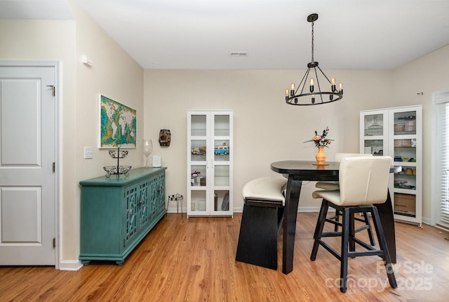 dining room with light wood-type flooring, baseboards, a notable chandelier, and visible vents