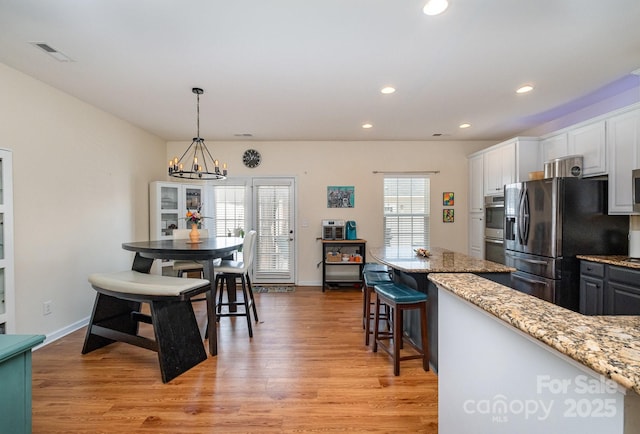 kitchen featuring light wood finished floors, stainless steel appliances, white cabinetry, and light stone counters