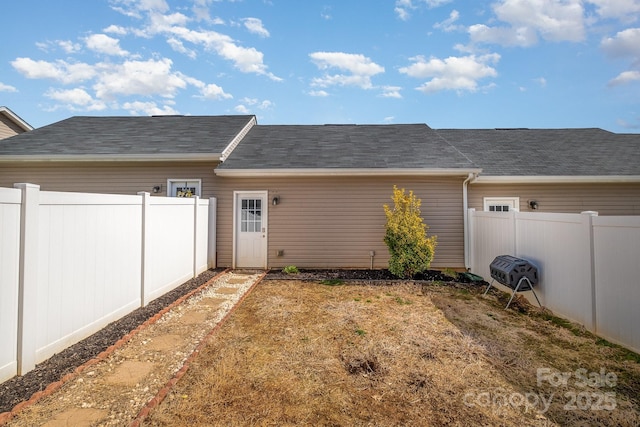 rear view of property with a fenced backyard and a shingled roof