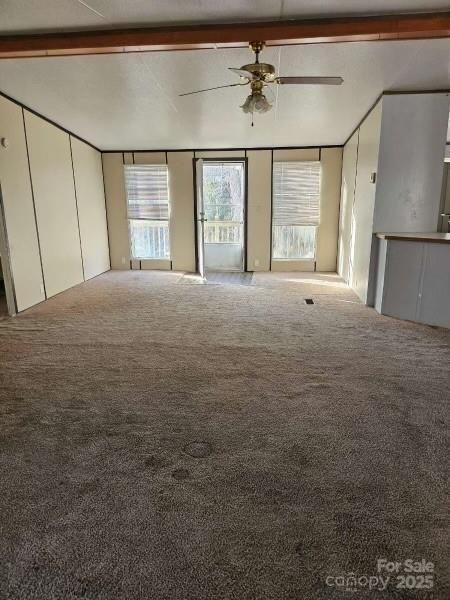 unfurnished living room with beamed ceiling, carpet flooring, and ceiling fan