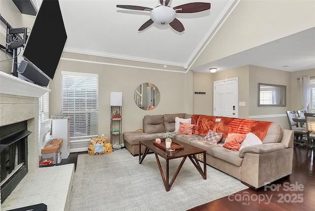 living room with crown molding, a fireplace, vaulted ceiling, ceiling fan, and wood finished floors