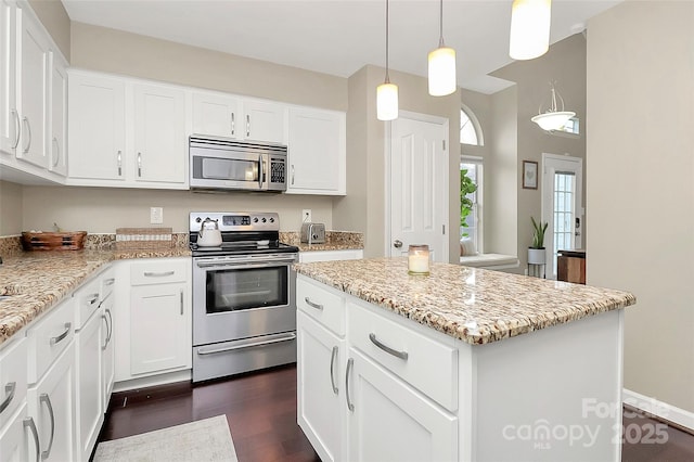 kitchen with appliances with stainless steel finishes, dark wood finished floors, white cabinets, and a kitchen island