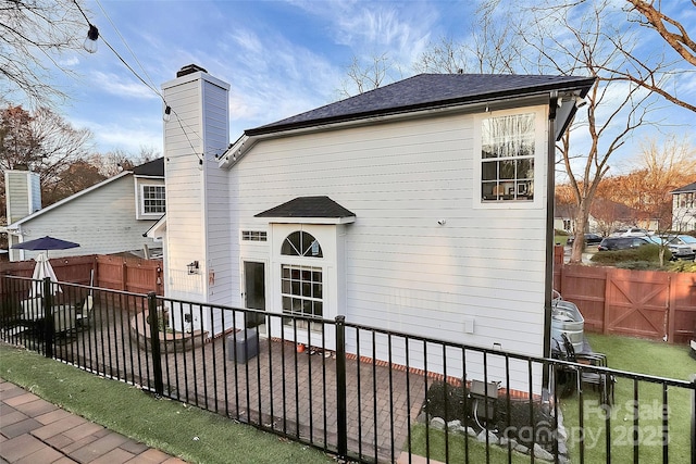 rear view of house featuring a fenced backyard, a chimney, and a shingled roof