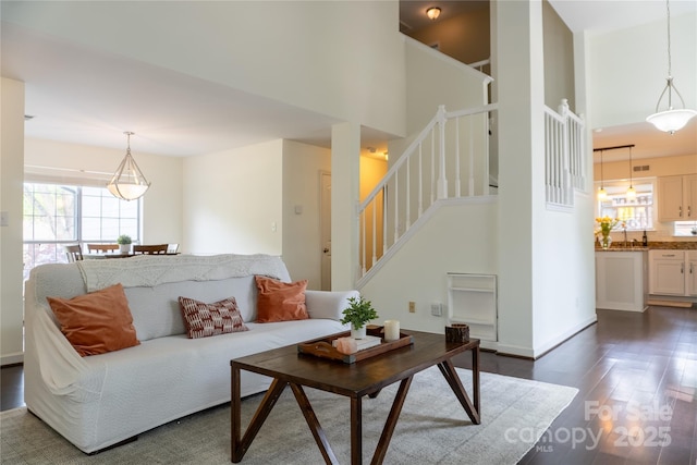 living area with plenty of natural light, a towering ceiling, dark wood-type flooring, and stairway