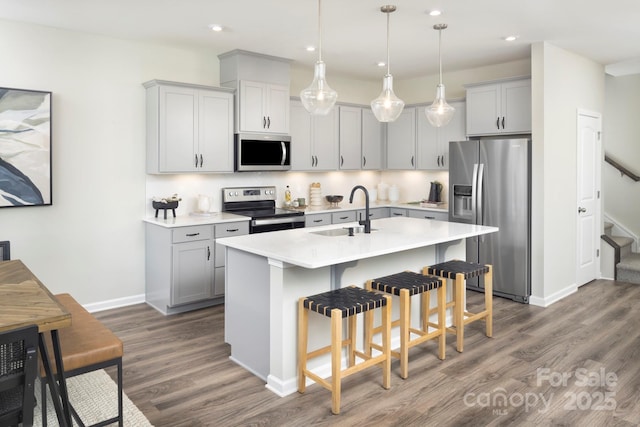 kitchen featuring sink, decorative light fixtures, dark hardwood / wood-style flooring, stainless steel appliances, and a kitchen island with sink