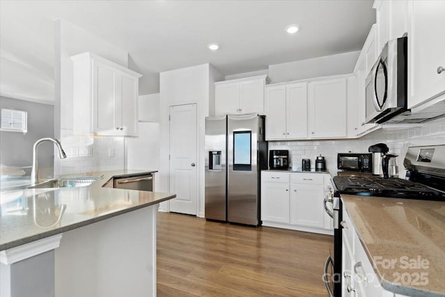 kitchen featuring white cabinets, appliances with stainless steel finishes, wood finished floors, a peninsula, and a sink