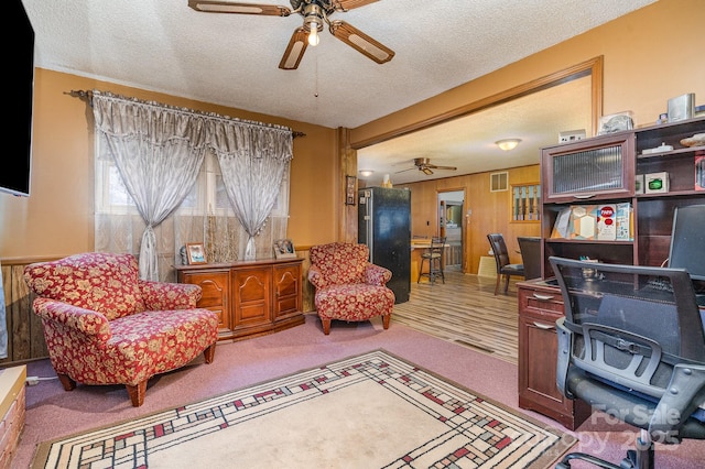 carpeted home office featuring ceiling fan, a textured ceiling, and wood walls