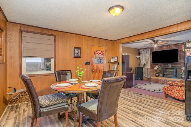 dining room with light wood-type flooring, a textured ceiling, a fireplace, and wood walls