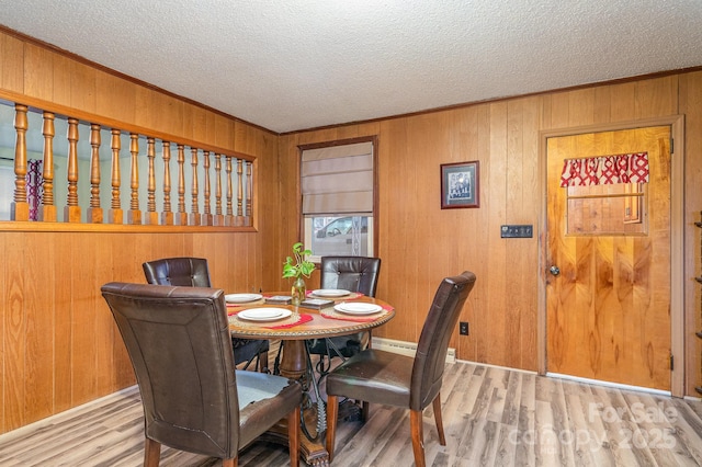 dining space with crown molding, wood walls, a textured ceiling, and light wood-type flooring