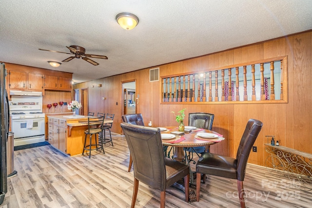 dining area with ceiling fan, wood walls, a textured ceiling, and light wood-type flooring