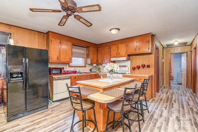 kitchen with white appliances, light hardwood / wood-style flooring, wooden walls, and a textured ceiling