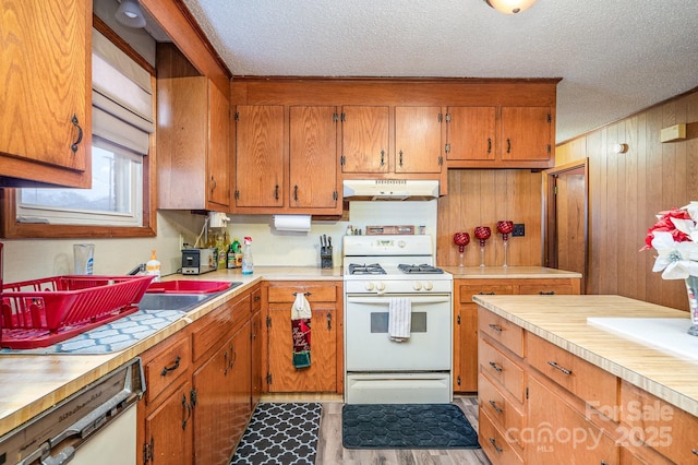 kitchen featuring wooden walls, a textured ceiling, white appliances, and light hardwood / wood-style floors