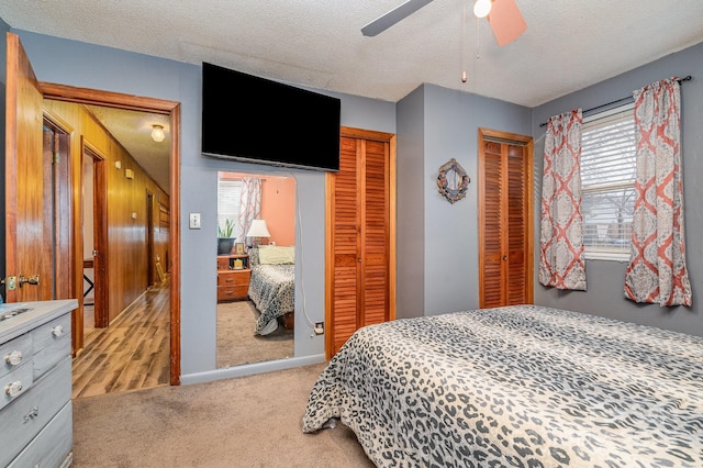 bedroom featuring ceiling fan, multiple closets, light colored carpet, and a textured ceiling