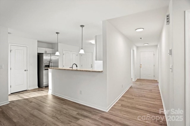 kitchen with white cabinetry, stainless steel fridge with ice dispenser, hanging light fixtures, light hardwood / wood-style flooring, and kitchen peninsula