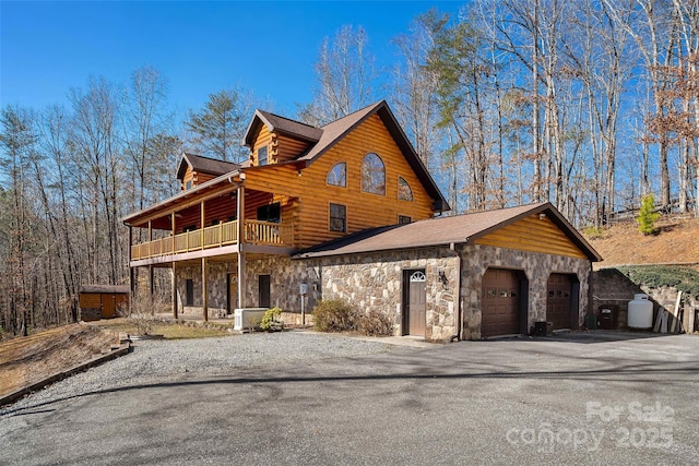 view of front facade featuring a balcony, stone siding, log siding, an attached garage, and central AC