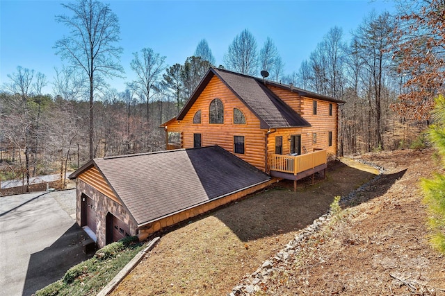 rear view of house featuring a garage, roof with shingles, a wooden deck, and log siding