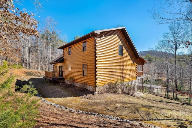 view of home's exterior featuring log exterior, a wooden deck, and a view of trees