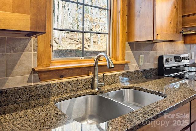 kitchen featuring decorative backsplash, dark stone counters, a healthy amount of sunlight, stainless steel range with electric stovetop, and a sink