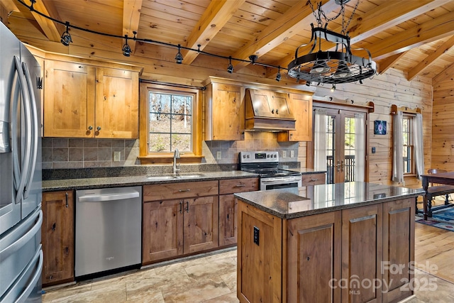 kitchen featuring premium range hood, a kitchen island, a sink, hanging light fixtures, and appliances with stainless steel finishes