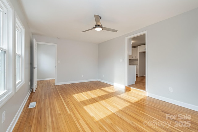 spare room with light wood-type flooring, visible vents, ceiling fan, and baseboards