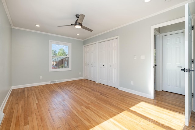 unfurnished bedroom with multiple closets, wood-type flooring, ornamental molding, and ceiling fan