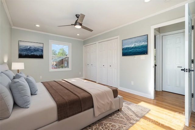 bedroom featuring baseboards, ornamental molding, light wood-style floors, two closets, and recessed lighting