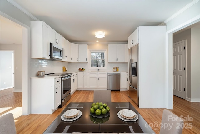 kitchen with light wood finished floors, appliances with stainless steel finishes, a sink, light countertops, and backsplash