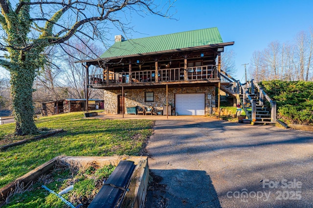 back of property with driveway, stone siding, metal roof, an attached garage, and stairs