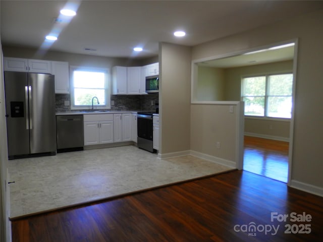 101 Colony Acres Dr, Charlotte, NC 28217 - kitchen featuring appliances with stainless steel finishes, a sink, light wood finished floors, white cabinetry, and tasteful backsplash
