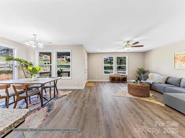 living area with ceiling fan with notable chandelier, baseboards, and wood finished floors