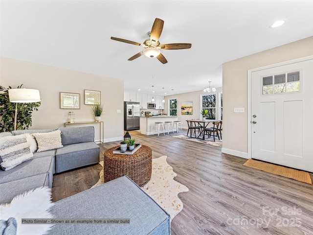 living area with recessed lighting, baseboards, light wood-style floors, and ceiling fan with notable chandelier
