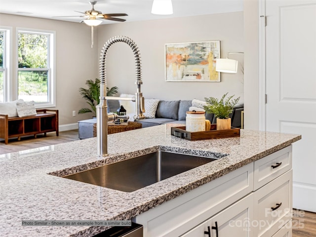 kitchen with light stone countertops, open floor plan, white cabinetry, a ceiling fan, and a sink